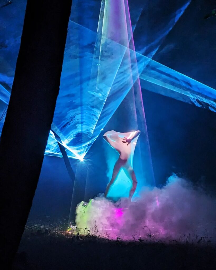 Person trapped in mesh dancing, surrounded by beams of colored light in forest